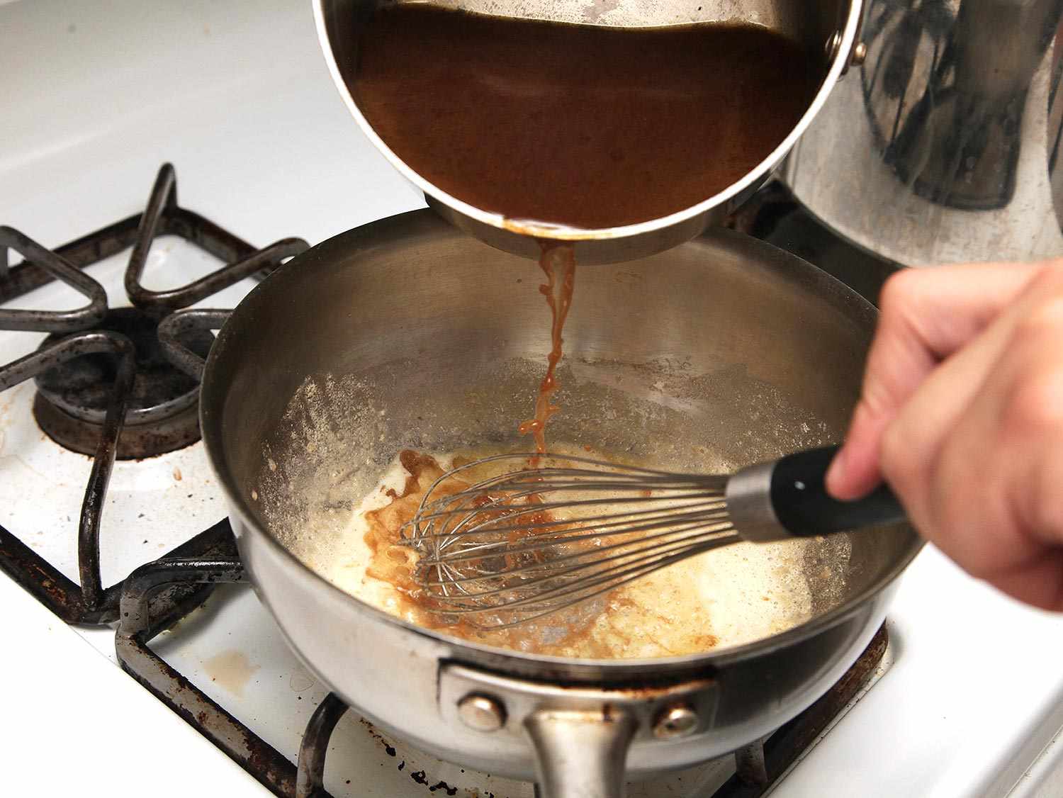 Adding strained turkey braising liquid into a saucepan with roux. 