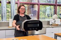 A person places the Ooni Volt 12 Electric Pizza Oven onto a table