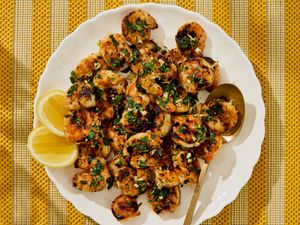 Grilled shrimp garnished with herbs next to lemon wedges on a plate