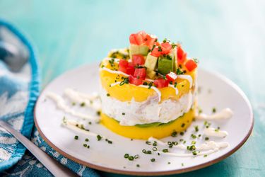 Layered dish of yellow mashed potatoes and tuna salad topped with diced tomatoes and avocados