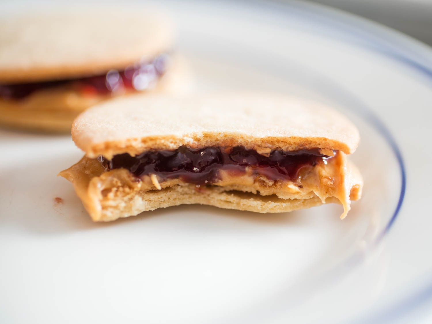 Profile closeup of a PB&J sandwich cookie that's been bitten in half, revealing the gooey layers of filling.
