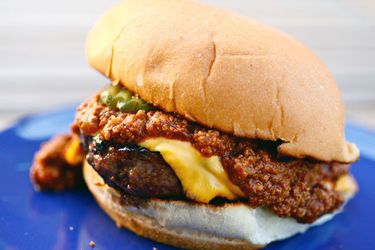 Closeup of a chili cheeseburger on a blue plate. Chili is dripping everywhere.