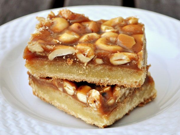 Closeup of two slices of salted cashew caramel bars, stacked together on a small white plate.