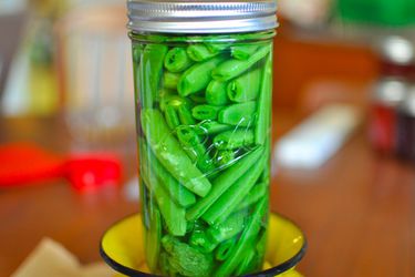 Closeup of a sealed glass jar of pickled sugar snap peas set on top of inverted yellow colander