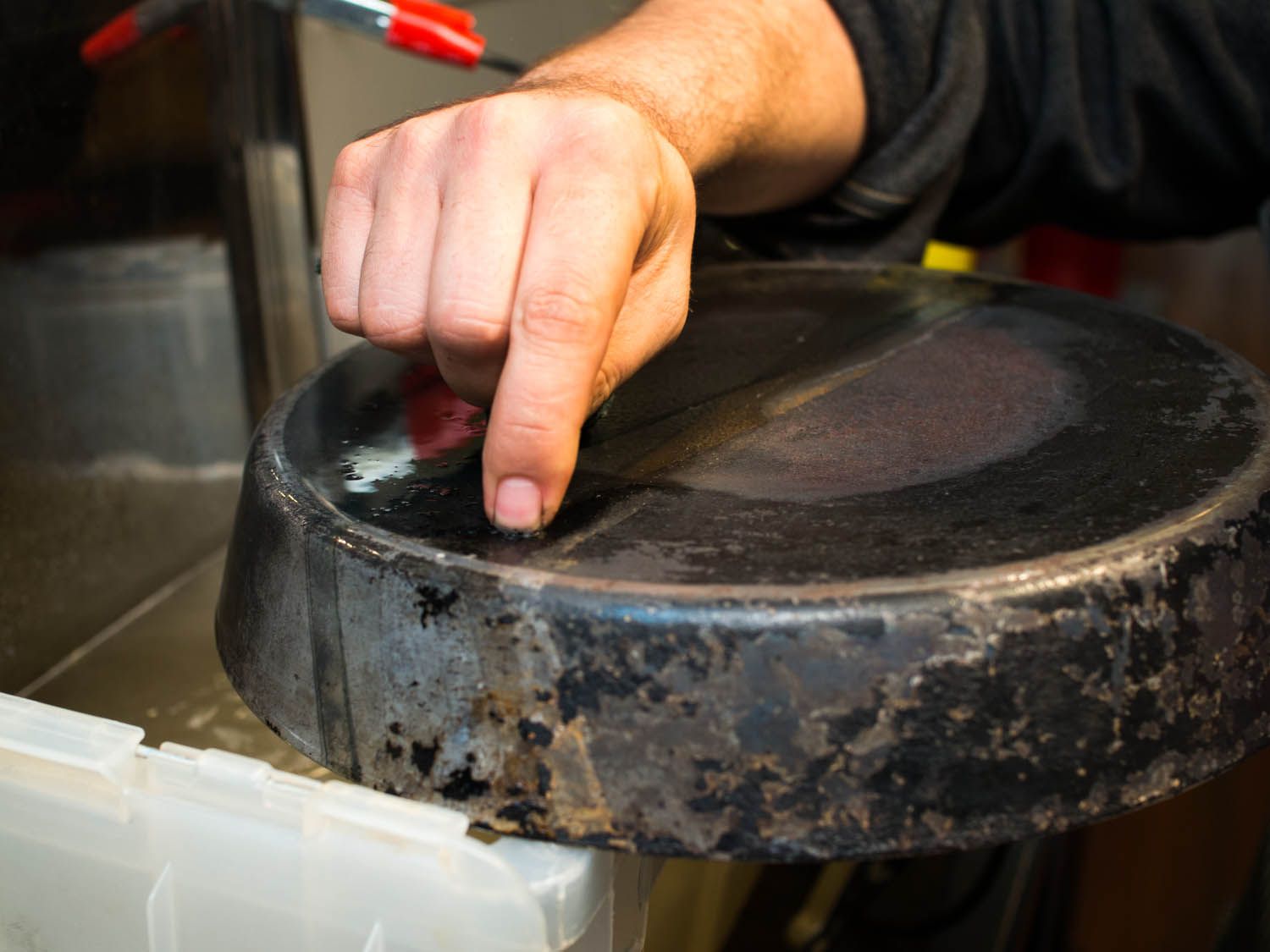 A finger scraping off rust and residue from the back side of a cast iron skillet.