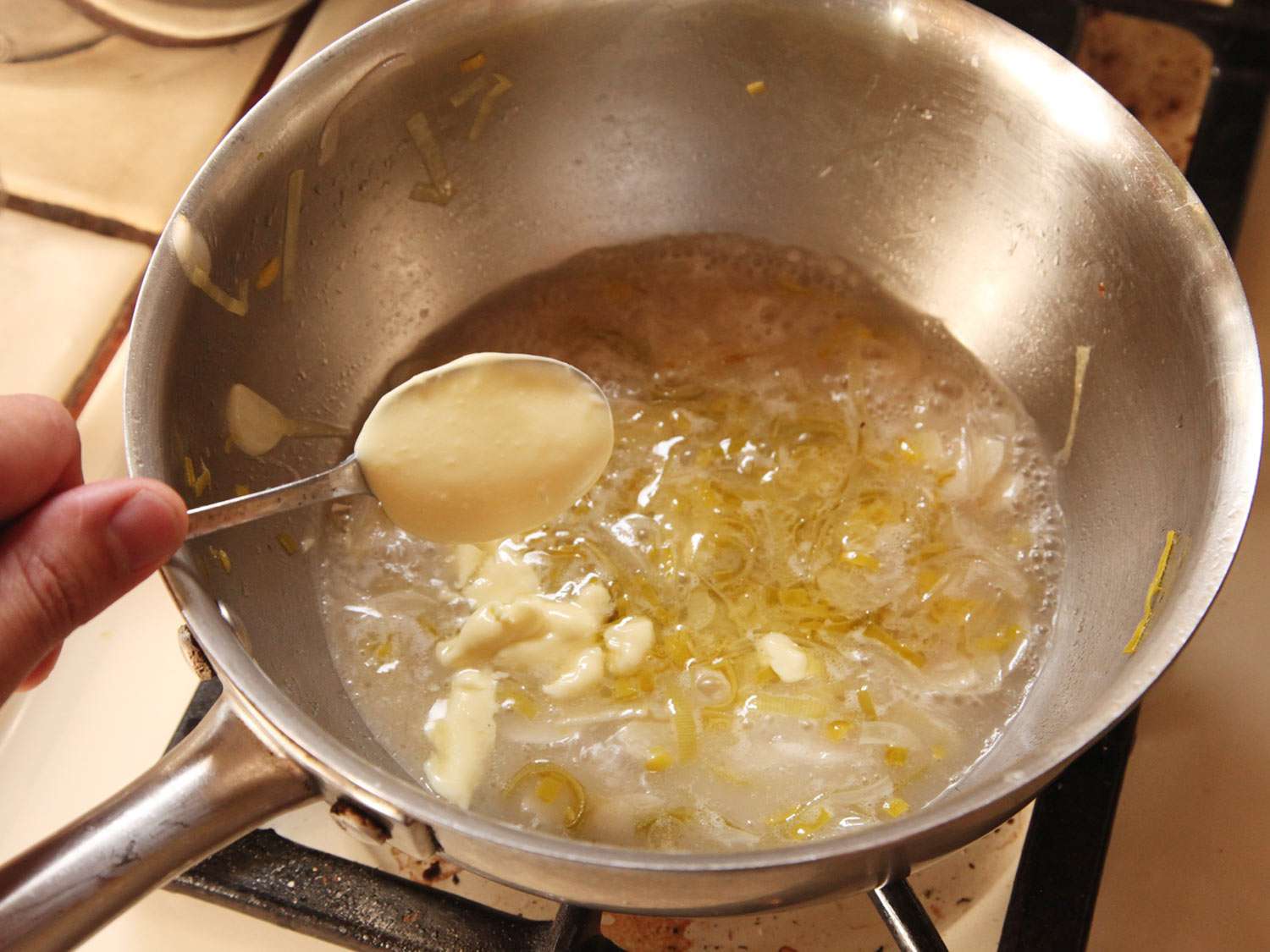 Author adding a generous spoonful of aïoli to the cooking liquid.
