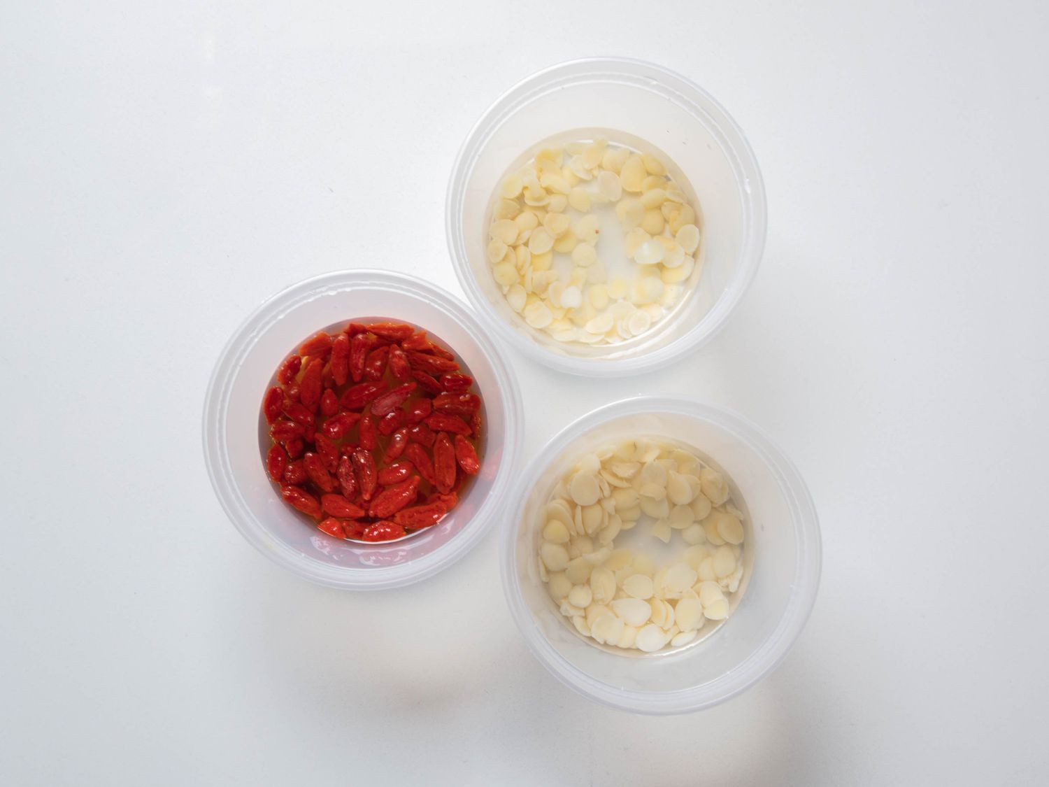Goji berries and almonds soaking in deli containers of water