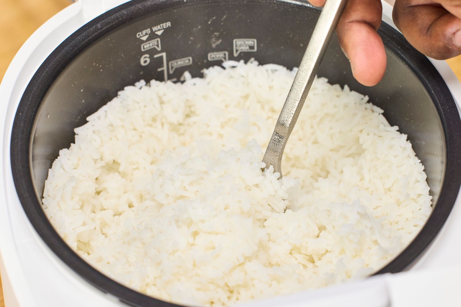 A person fluffs rice cooked in the Cuckoo 6-Cup Micom Rice Cooker