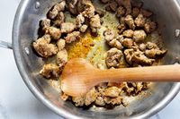 Cooked sausage pieces in a pan stirred with a Field Company Cherry Wood Spoon