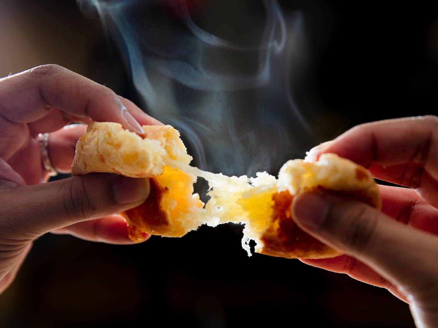 Hands pulling apart hot steaming cheesy bread.