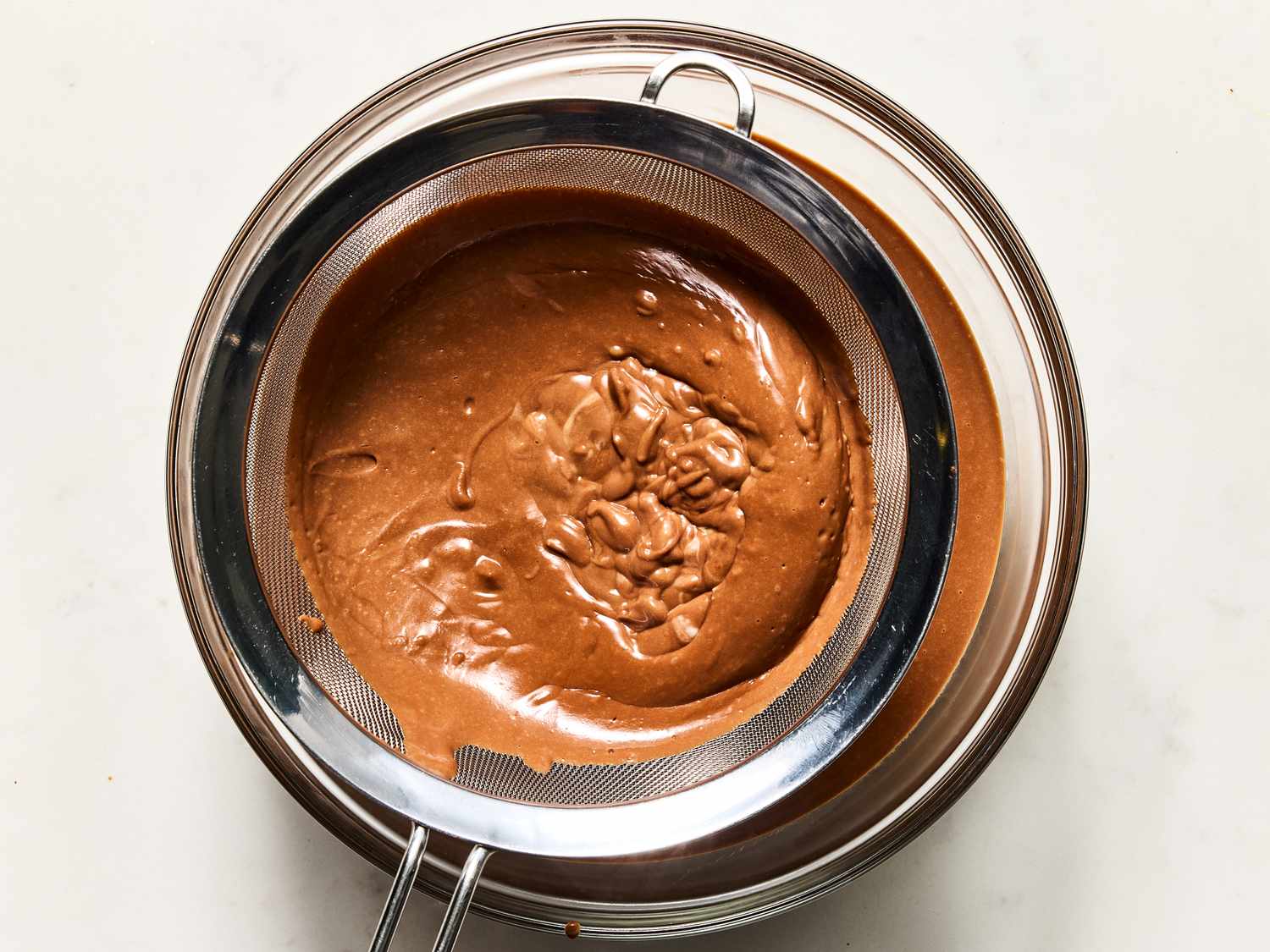 A bowl filled with chocolate banana pudding, being strained through a mesh sieve in preparation