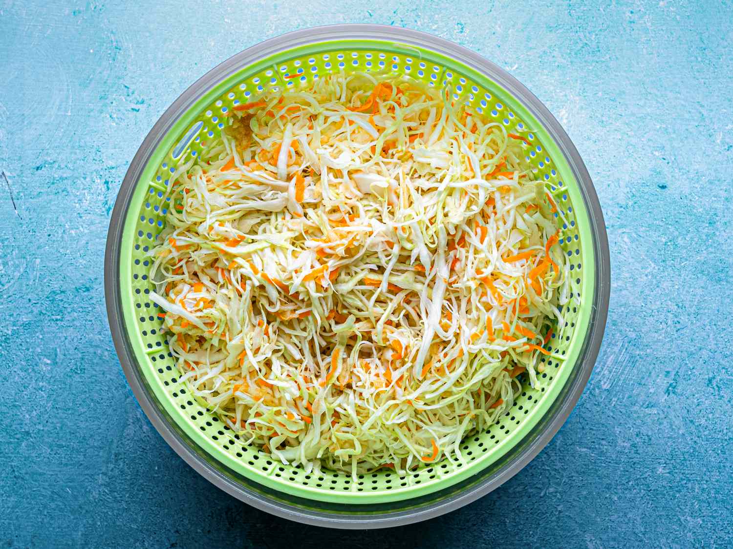 A green colander filled with coleslaw made of shredded cabbage carrots and apple