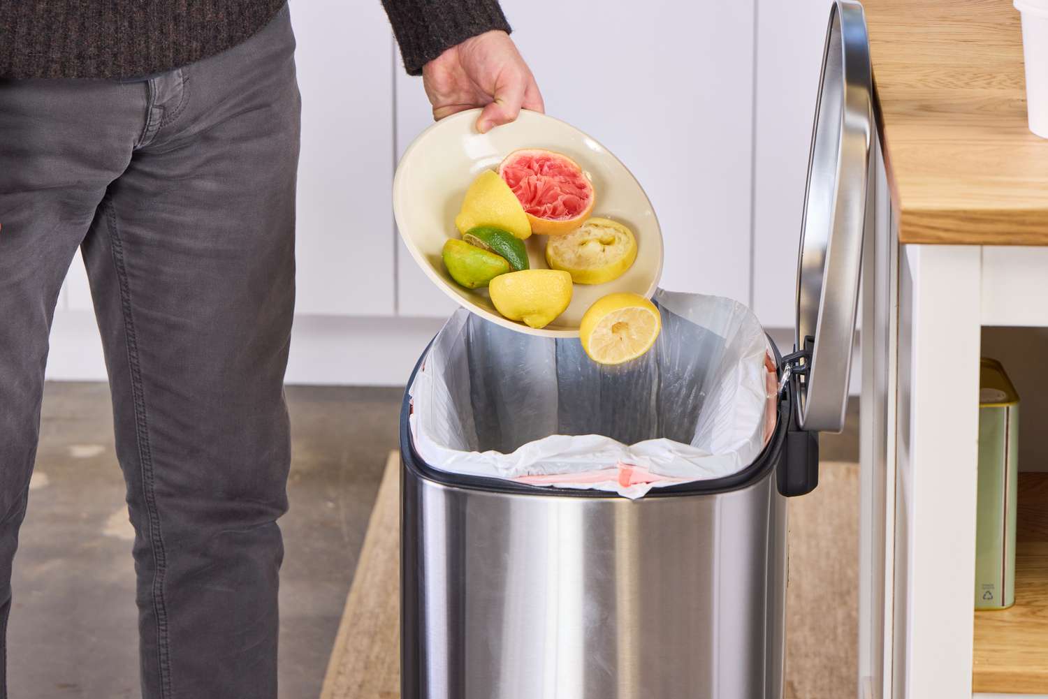 A person pours citrus fruit into the Amazon Basics 13.2 Gallon Soft-Close Trash Can with Foot Pedal