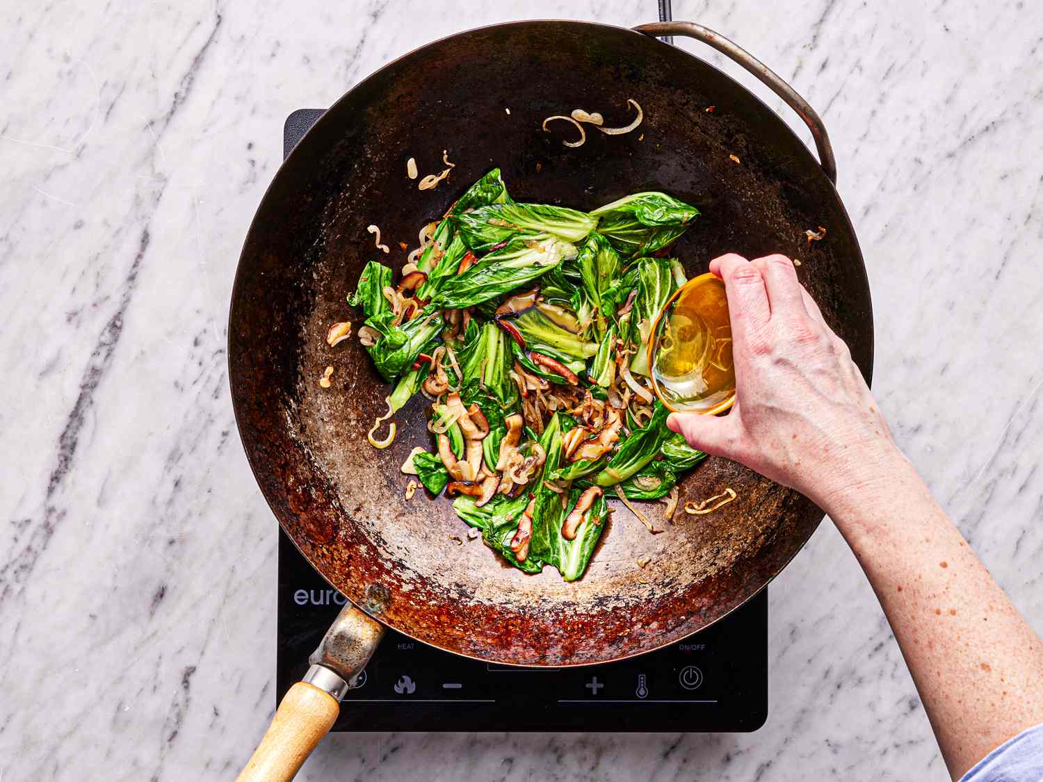 Overhead view of adding oil to bok choy in wok