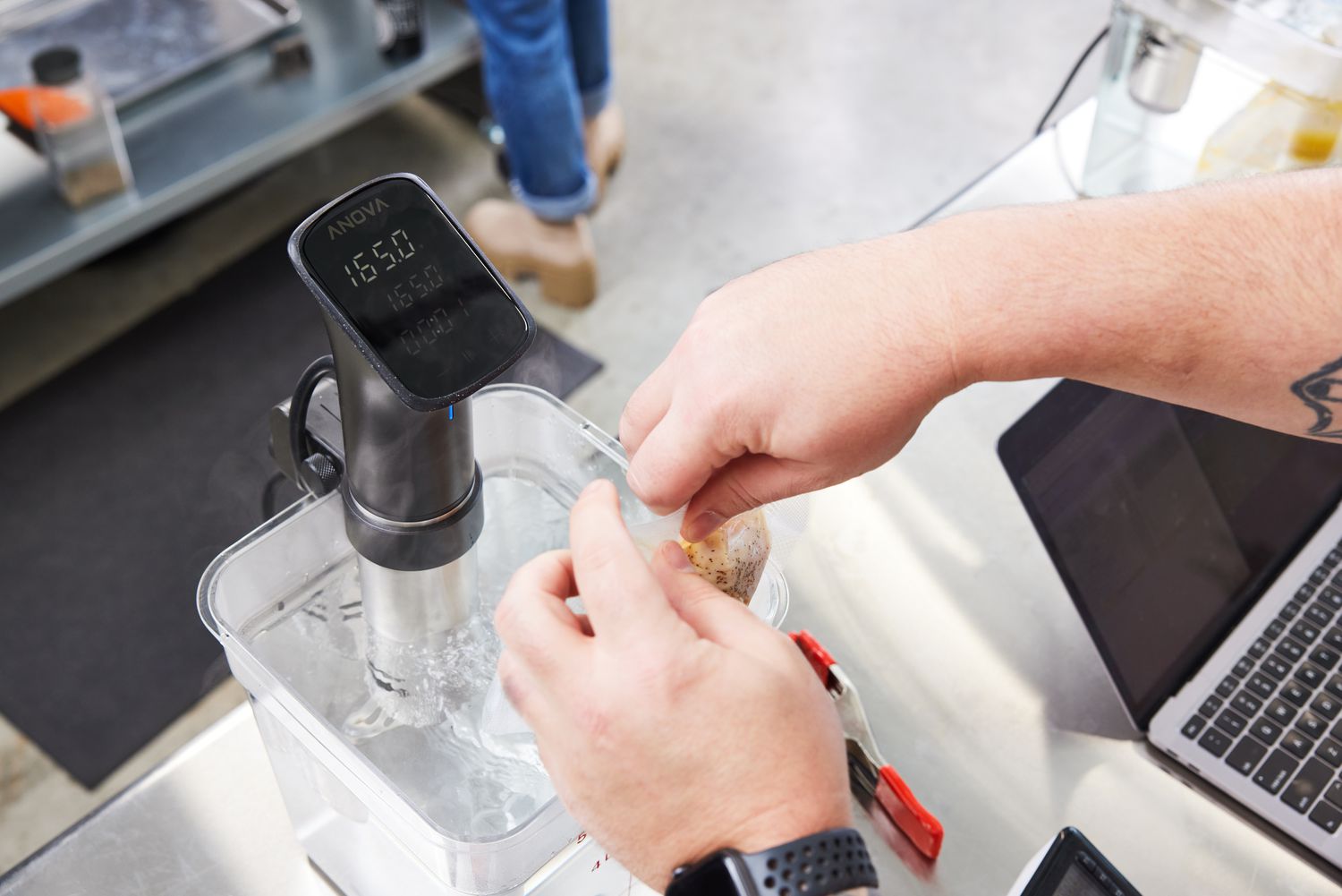 Hands adding a packet to a bucket of water with the Anova Culinary Precision Cooker Pro