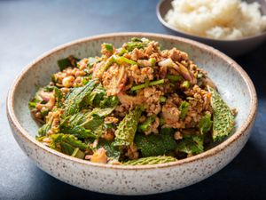 Serving bowl of pork laab with a bowl of sticky rice in the background