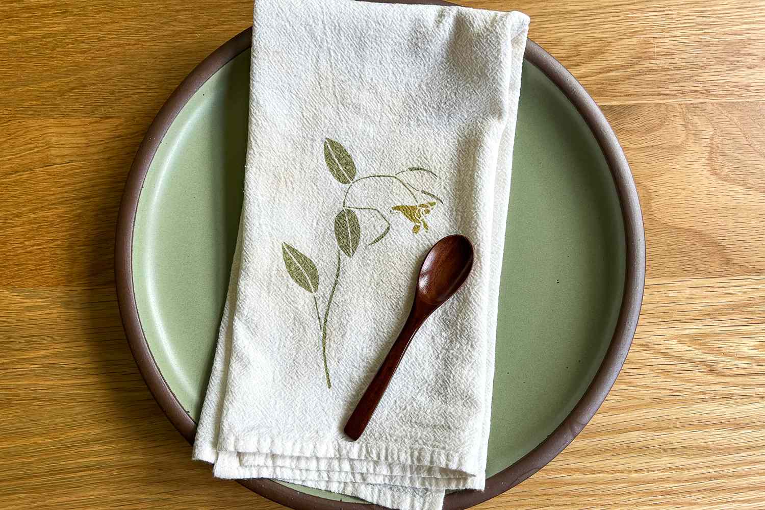 A ceramic plate with a cloth napkin and wooden spoon placed on top, featuring a leaf and flower pattern on the napkin