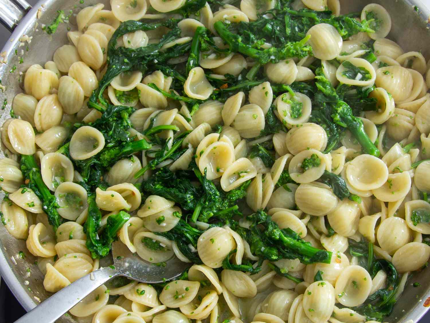 Tossing together cooked orecchiette, broccoli rabe, and anchovy base in a skillet.