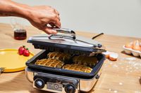 A square waffle maker being opened, to reveal four waffles inside