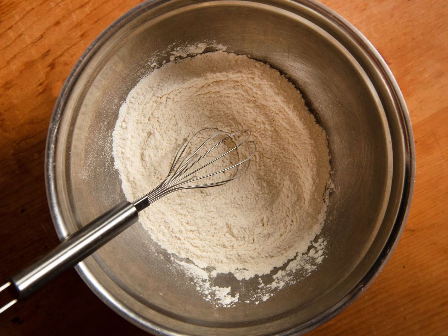 Whisking together flour, baking powder, and salt in a large metal bowl.