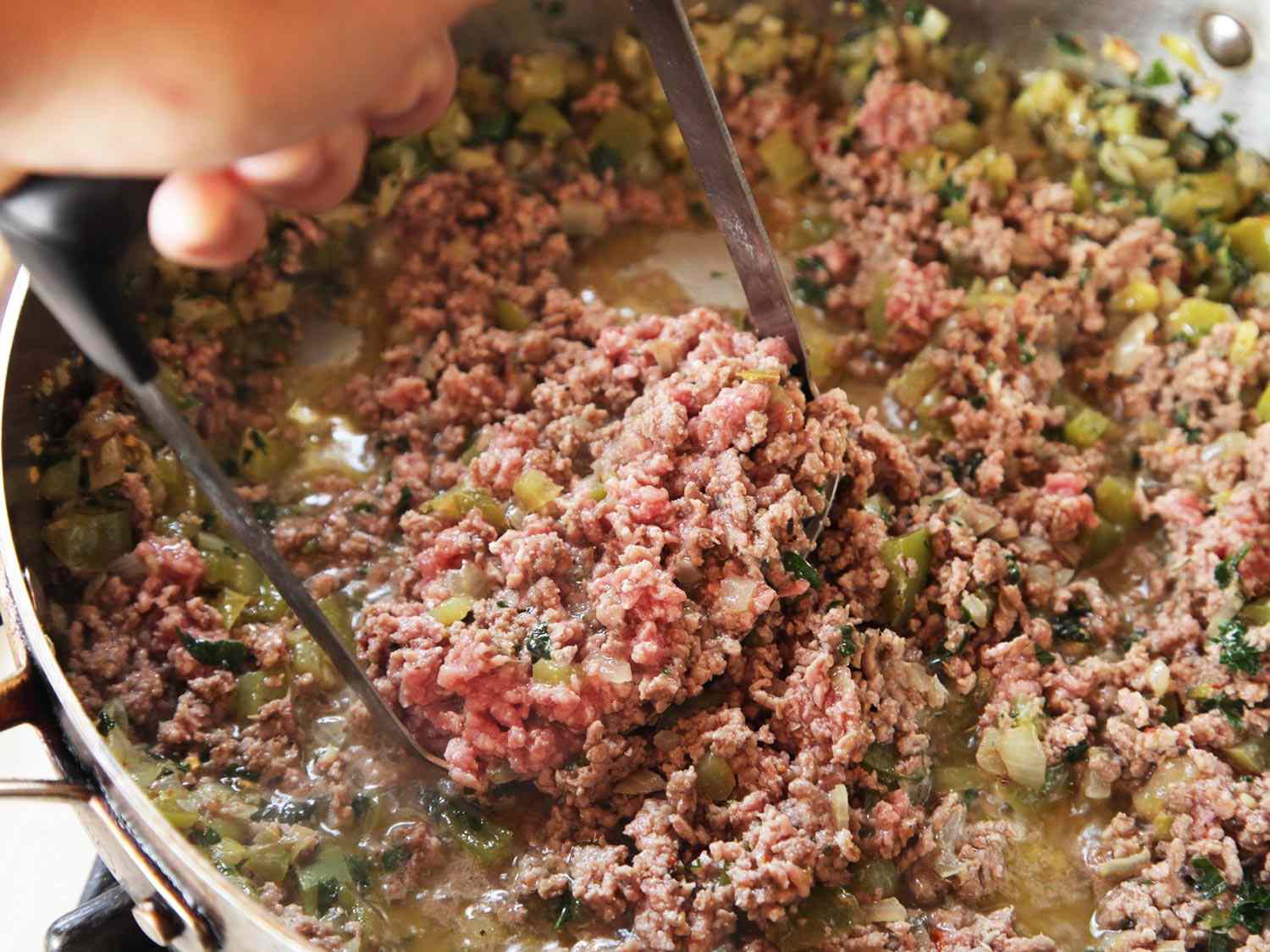 Close-up of author using a potato masher to further break up the ground beef.
