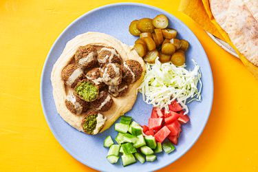 Plated pita bread stuffed with falafels, tahini, tomatoes, cucumber, pickles, and shredded cabbage