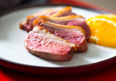 Medium-rare duck breast sliced and served on a plate with orange wedges