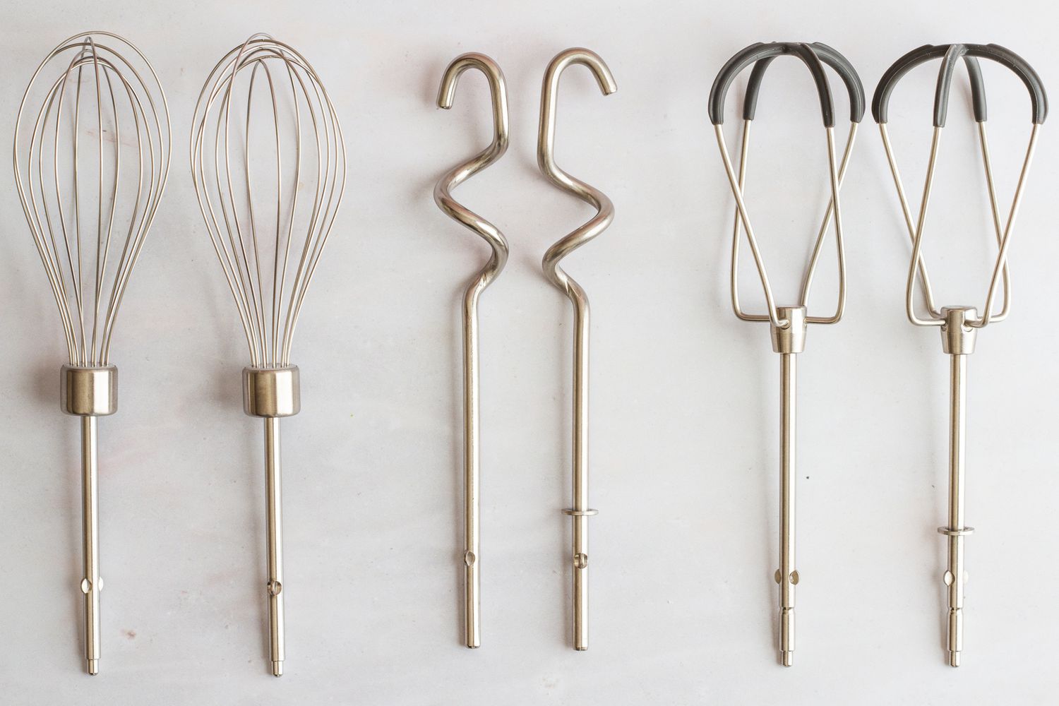 Three sets of hand mixer attachments on a grey surface.