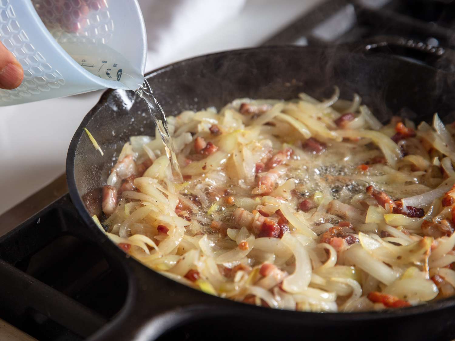 White wine is poured into the skillet of onions and bacon.