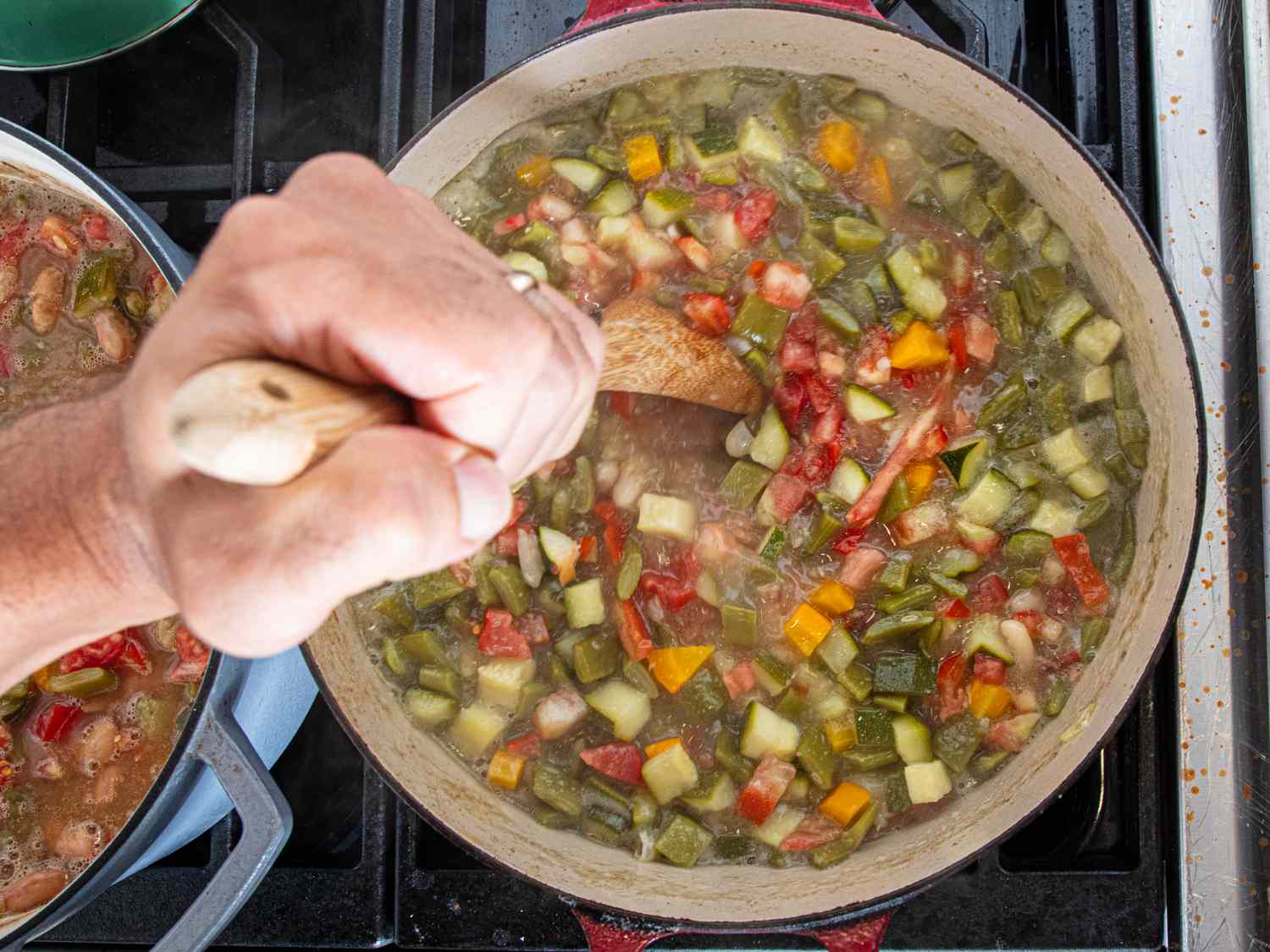 A hand stirring a vegetable stew in a pot on a stove