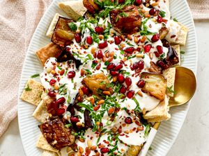 A plated serving of eggplant fatteh garnished with pomegranate seeds parsley and yogurt sauce