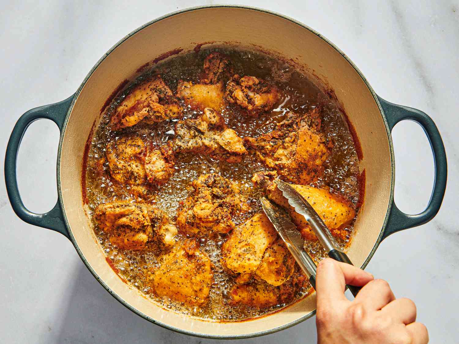 Fried chicken getting flipped and browned in oil in dutch oven 