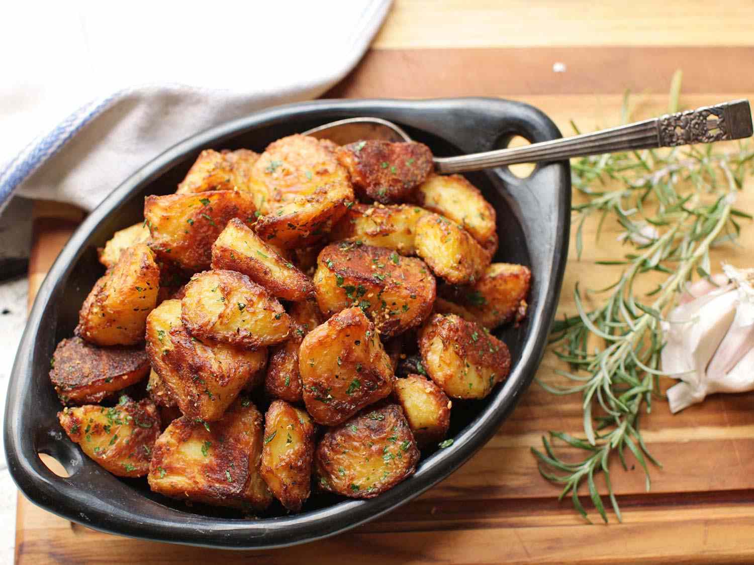 A black dish filled with golden crispy roasted potatoes. 