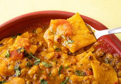 A spoonful of lentil curry with vegetables and garnished herbs being lifted from a bowl