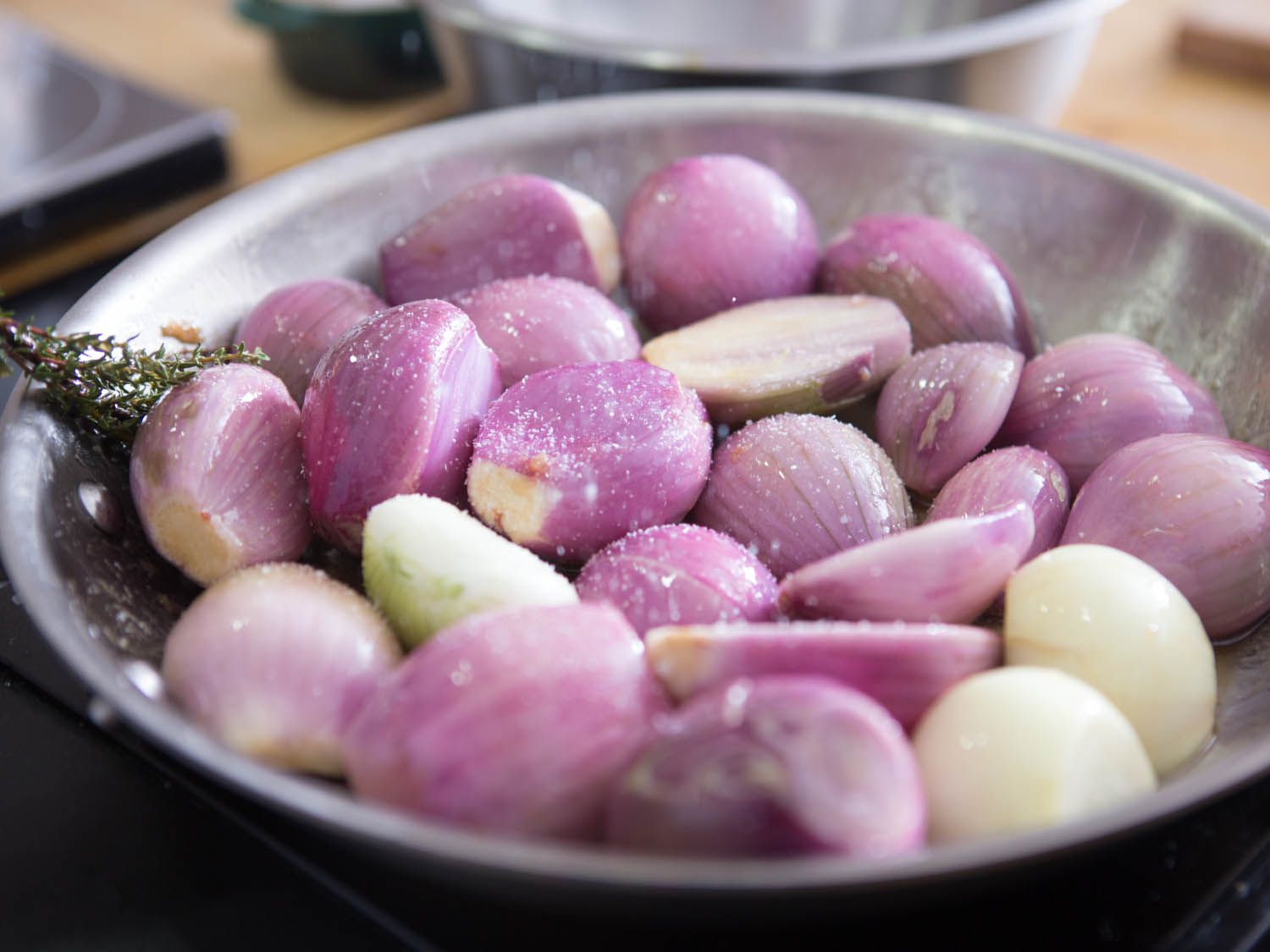 Sprinkling salt on whole peeled shallots and thyme sprigs in a saute pan.