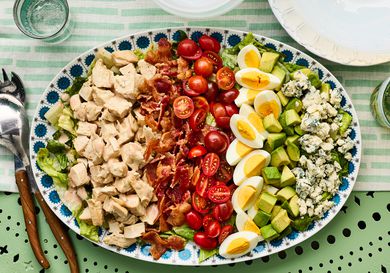 A Cobb salad served on a decorative platter, featuring rows of ingredients including chicken, bacon, cherry tomatoes, eggs, avocado, and blue cheese