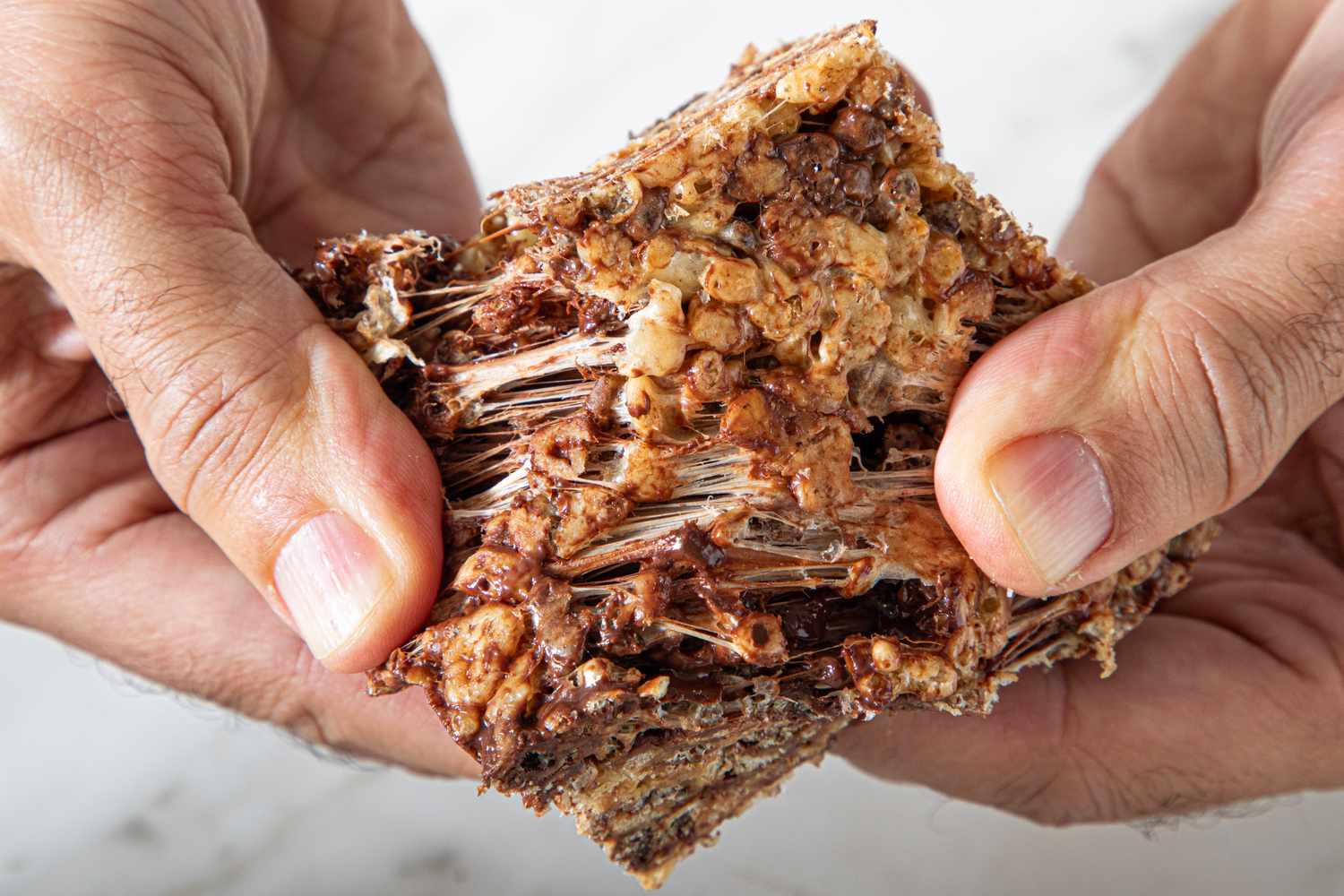 Hands pulling apart a sticky textured crispy rice treat