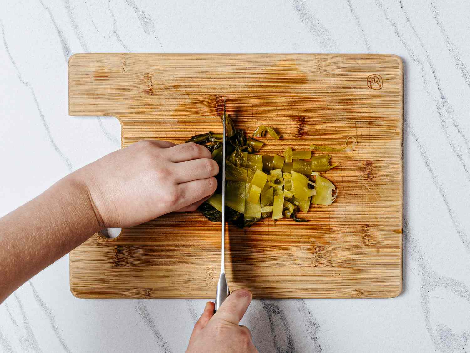 Mincing rinsed pickled mustard greens on a wooden cutting board 