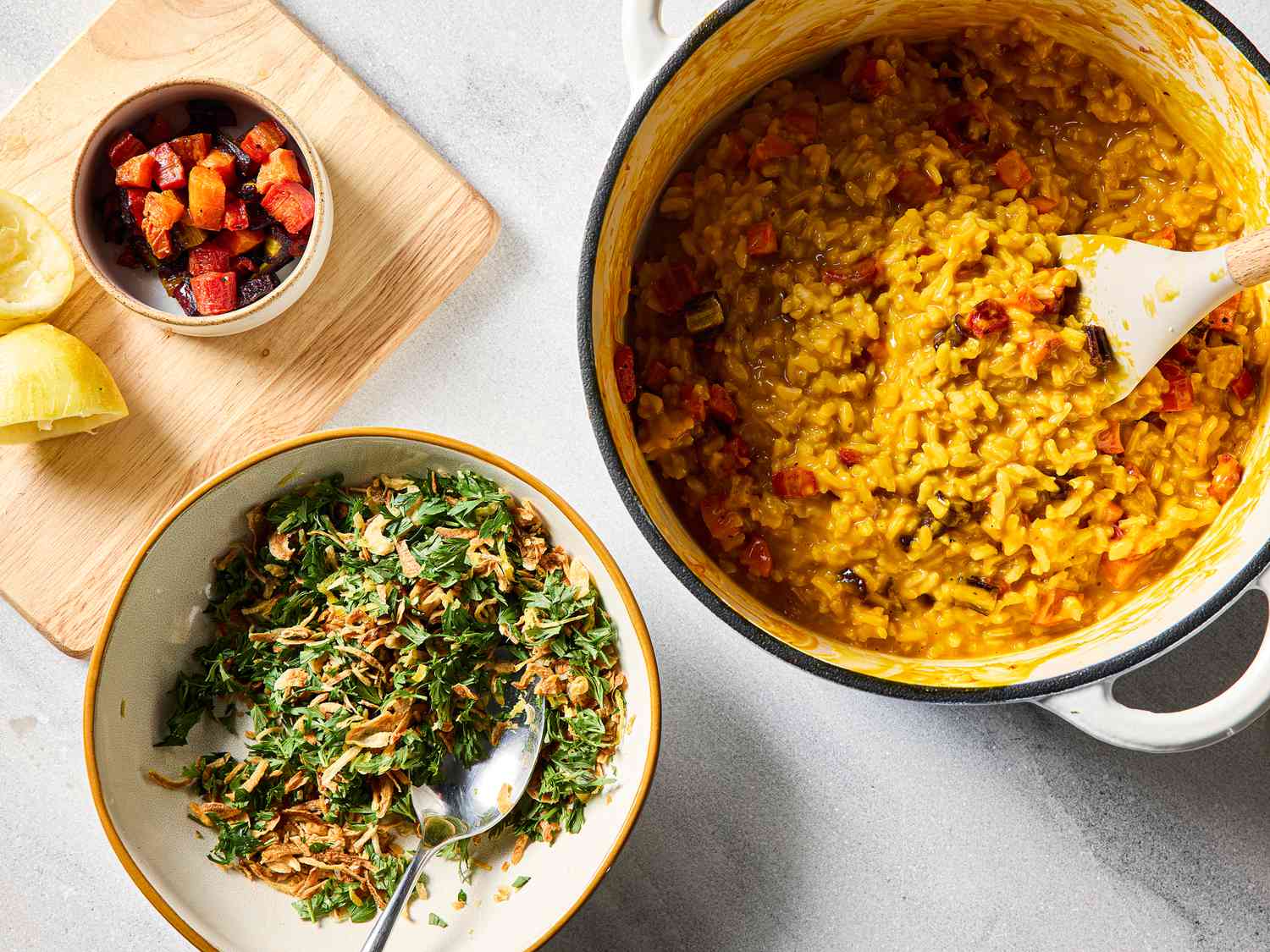 A pot of carrot risotto with a bowl of garnishes and lemon wedges on the side