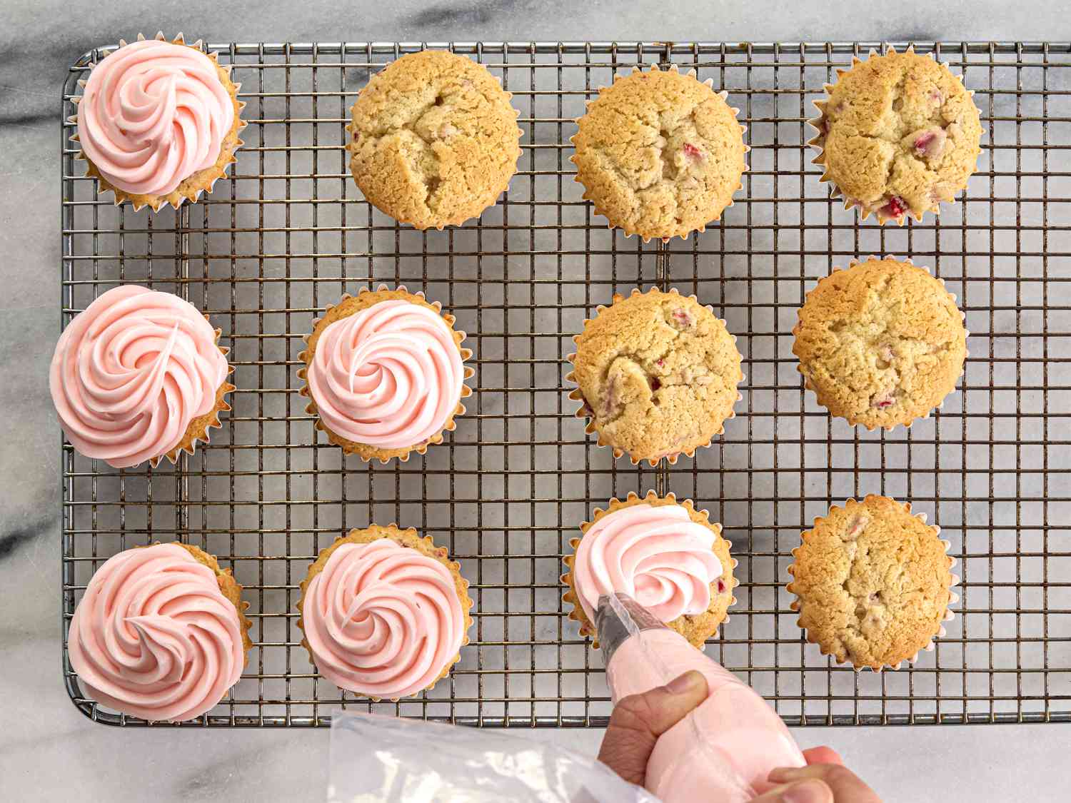 cupcakes being piped with frosting on a cooling rack 