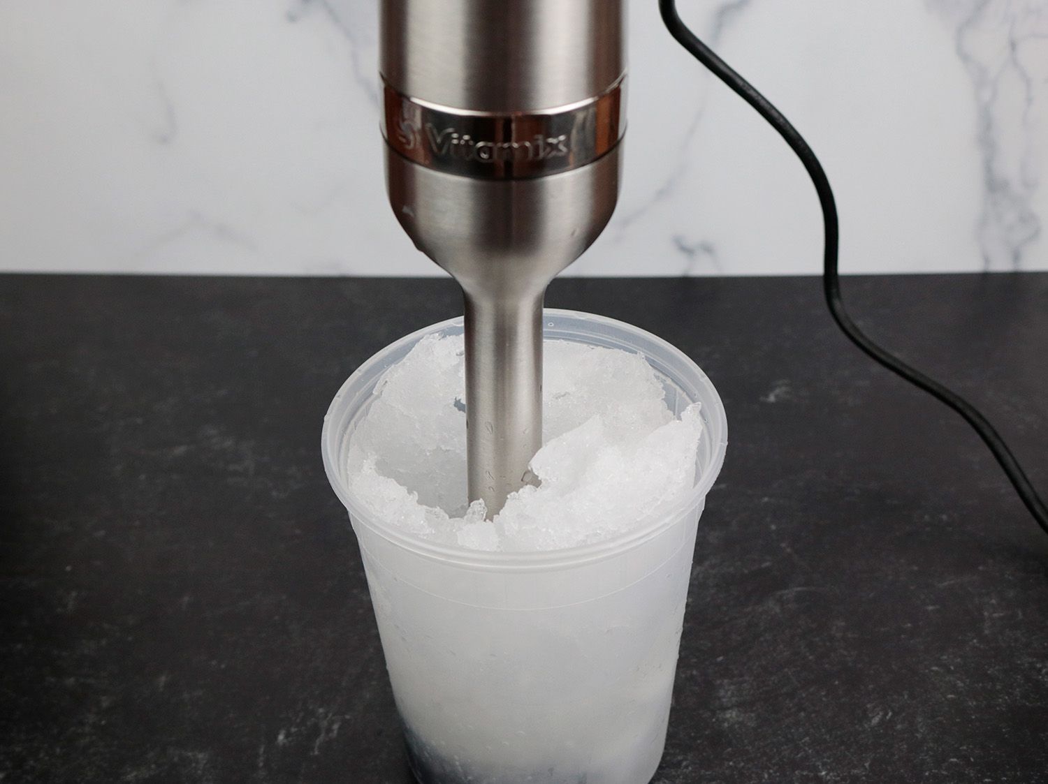 an immersion blending is immersed in a plastic container of ice and is blending it into slush