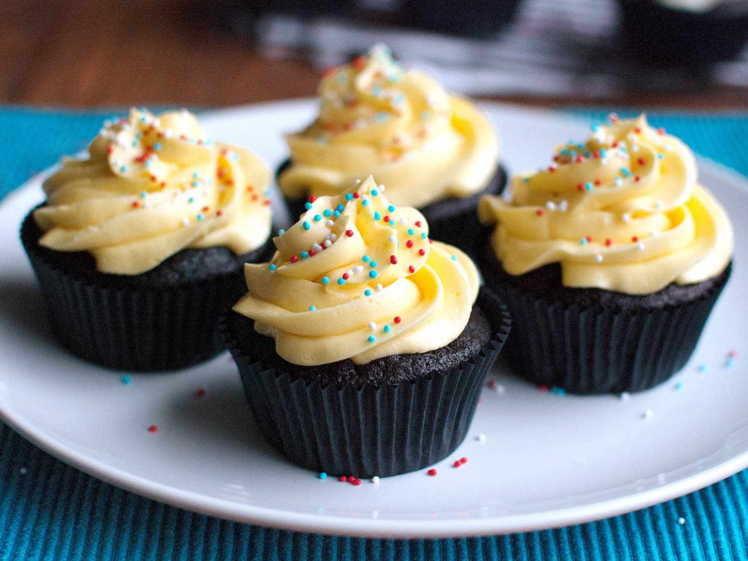 Four French buttercream cupcakes resting on a plate with sprinkles. 