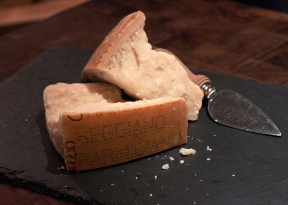 Wedges of Parmigiano-Reggiano on a black slate with a knife.