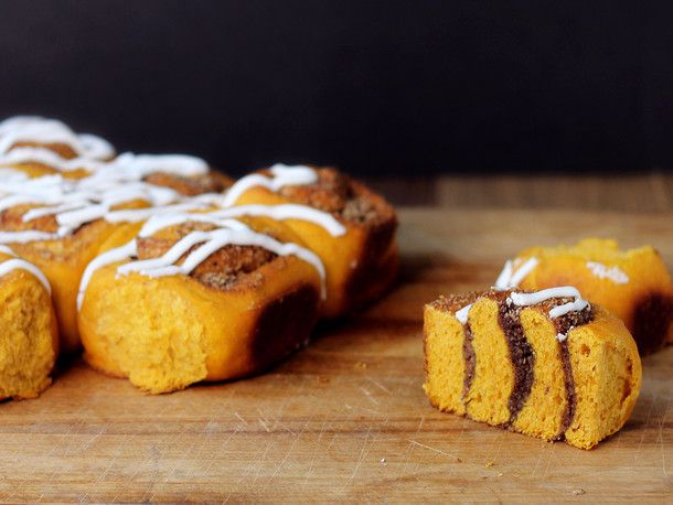 Pumpkin sweet swirl buns on a cutting board. One has been sliced in half to show the swirled layers of filling.