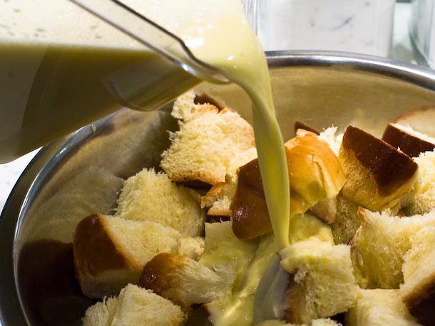 Pouring custard base over chunks of stale bread in a mixing bowl.