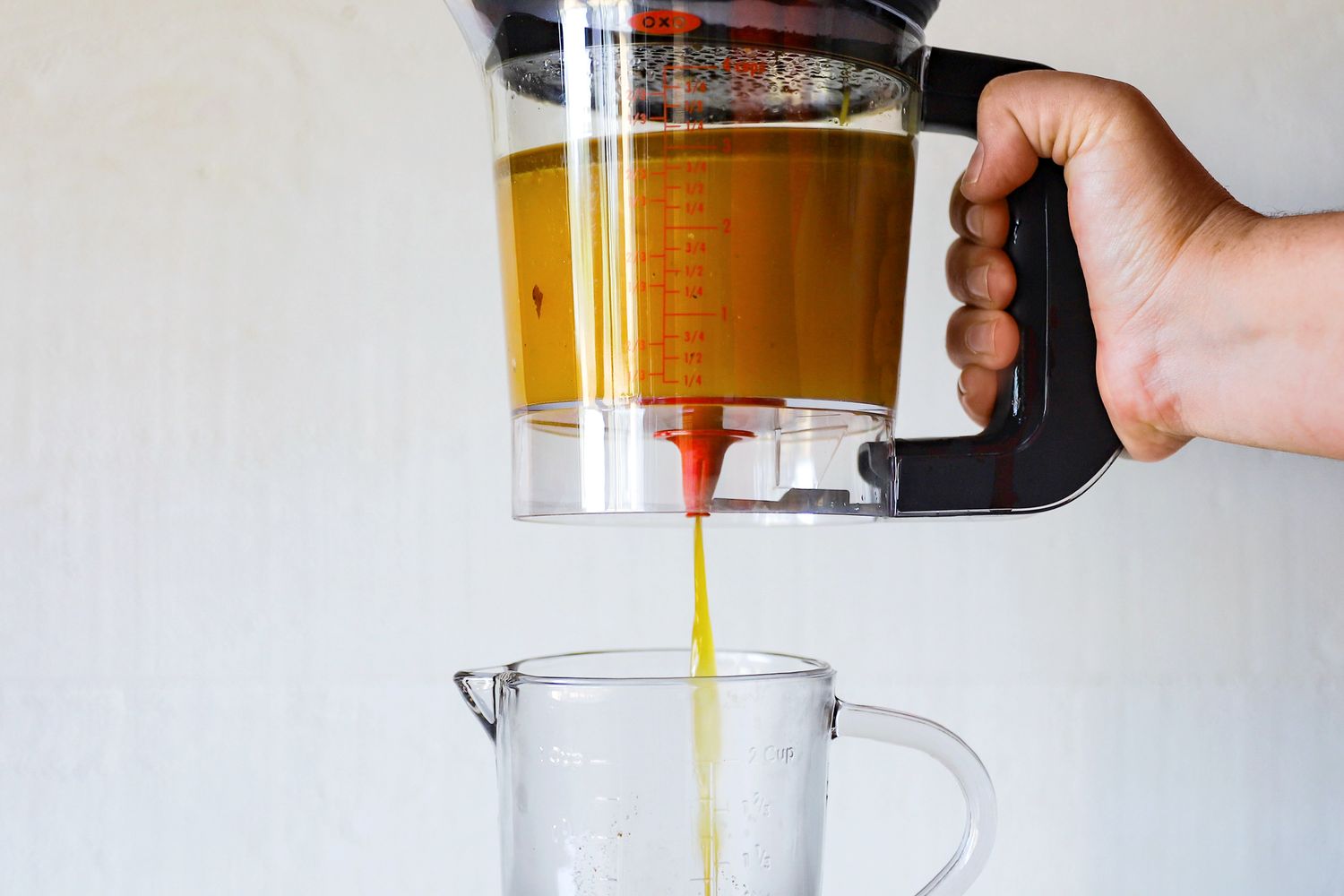 A hand holding a fat separator pouring liquid into a measuring cup below