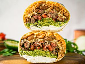 A stacked burrito crosssection showing fillings such as meat beans rice guacamole and cream cheese on a wooden surface