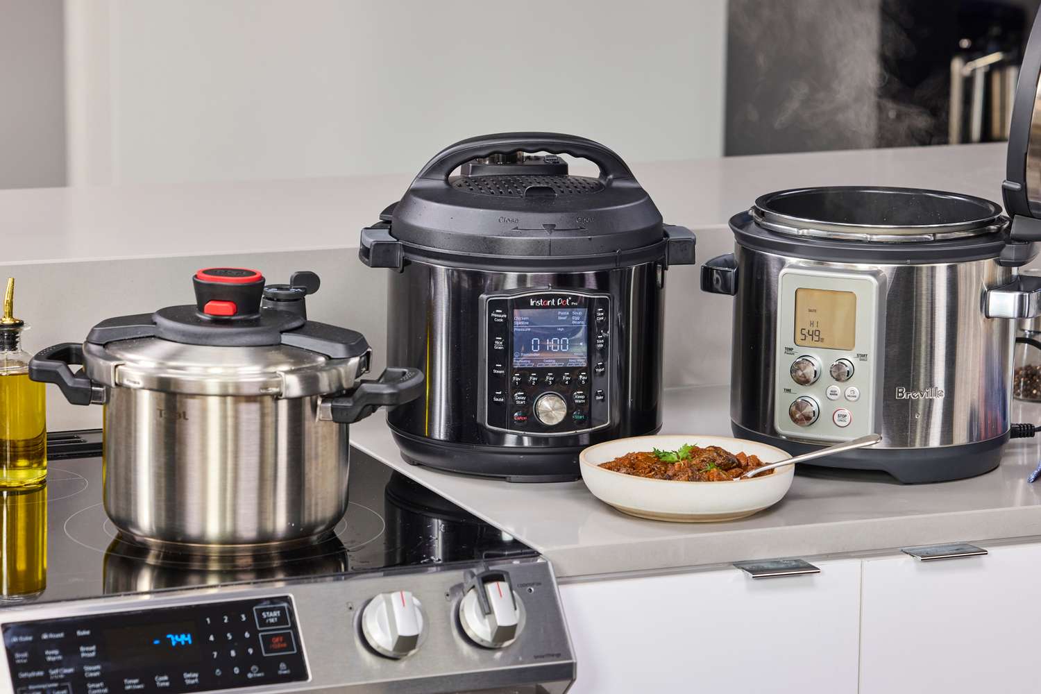 Three pressure cookers sitting on a kitchen counter with a bowl of cooked food in front of them