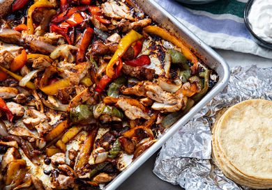 Sheet Pan chicken fajitas with a stack of tortillas nearby.
