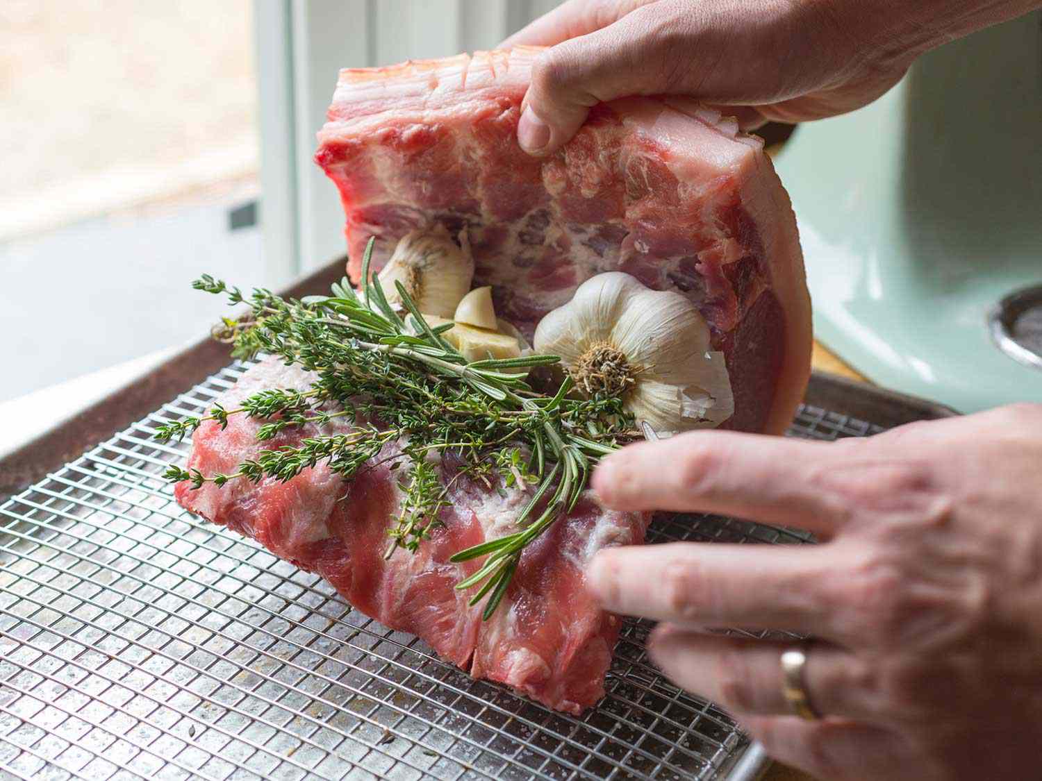 Folding a raw pork loin over cut heads of garlic and fresh herbs